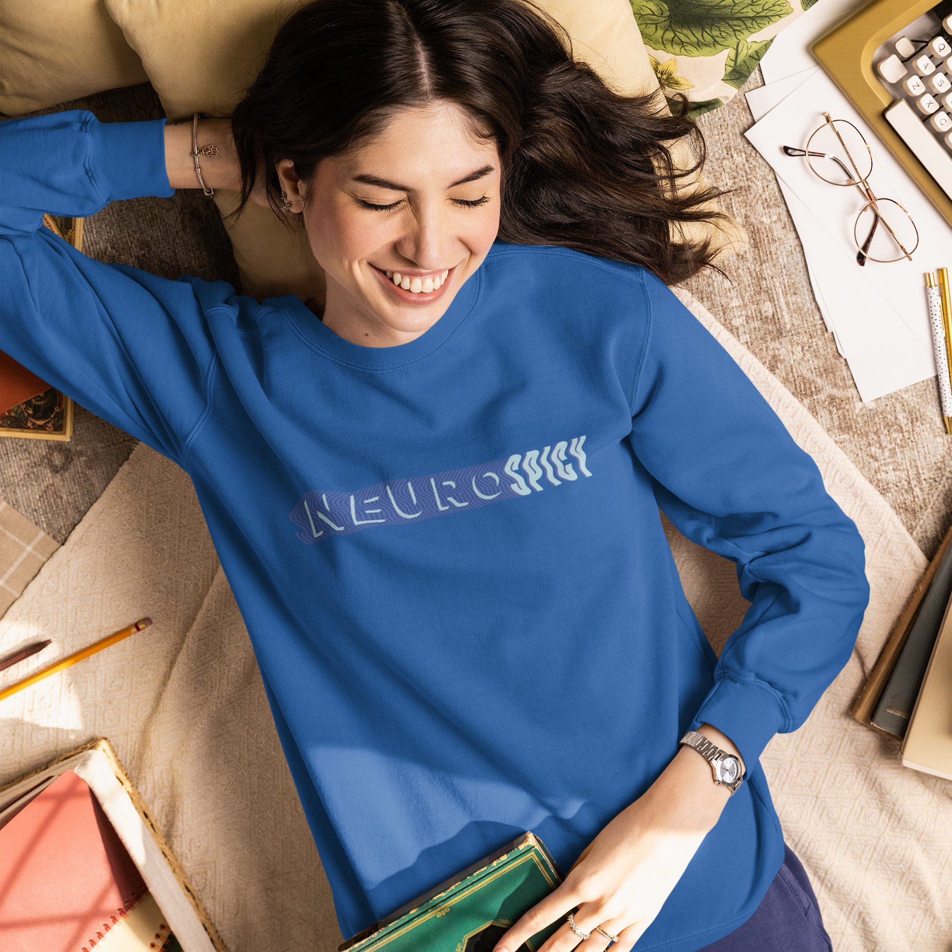 Woman wearing a blue sweatshirt with text, lying on a couch surrounded by books and papers.