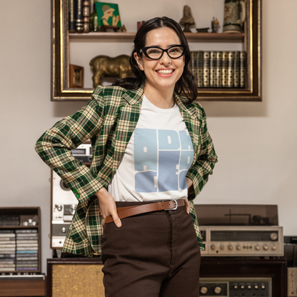 Person wearing a plaid shirt over a graphic t-shirt in a room with vintage record players and books.