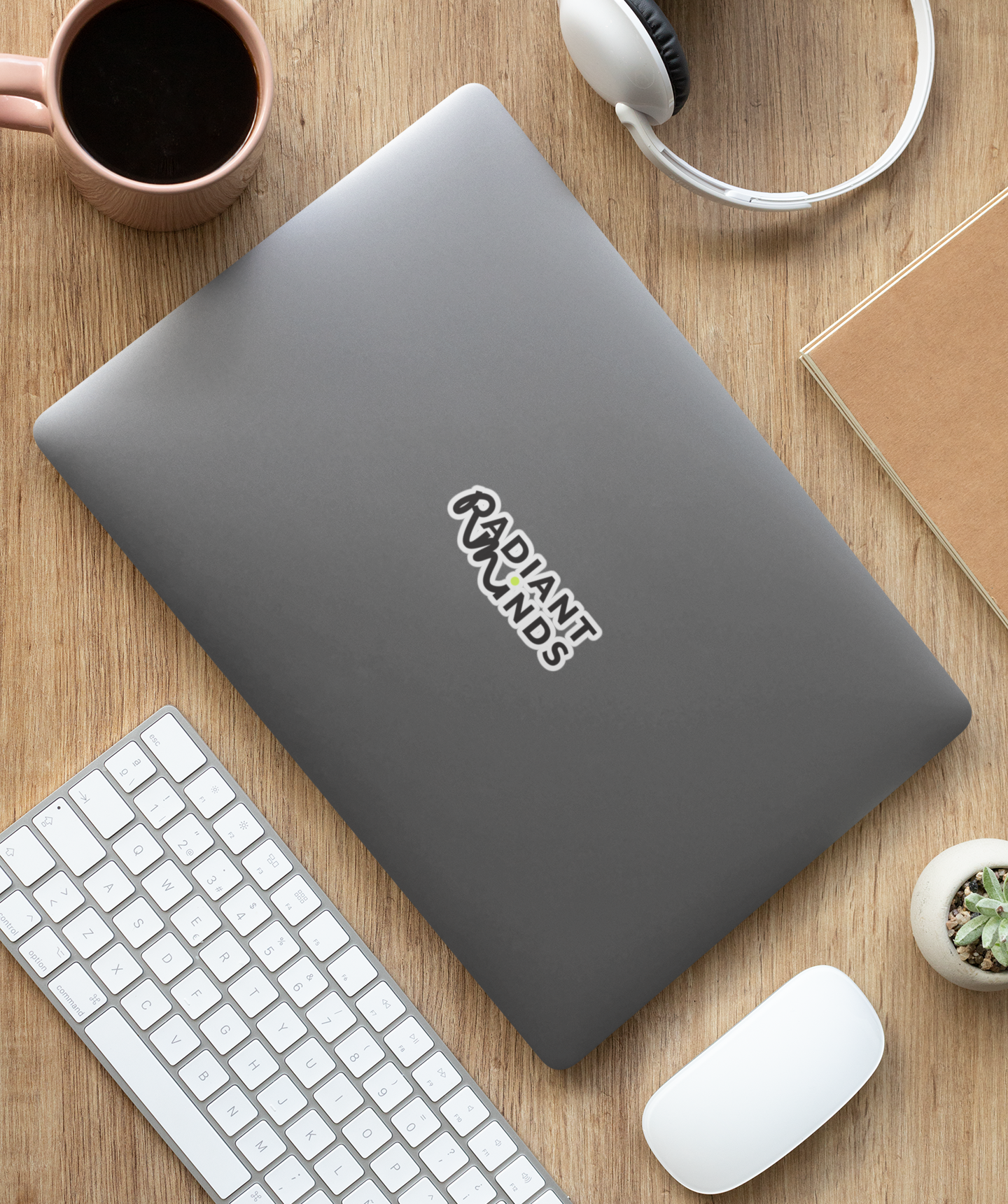 Gray laptop with 'RADIANT MINDS' logo on a wooden desk with keyboard, mouse, and coffee cup.