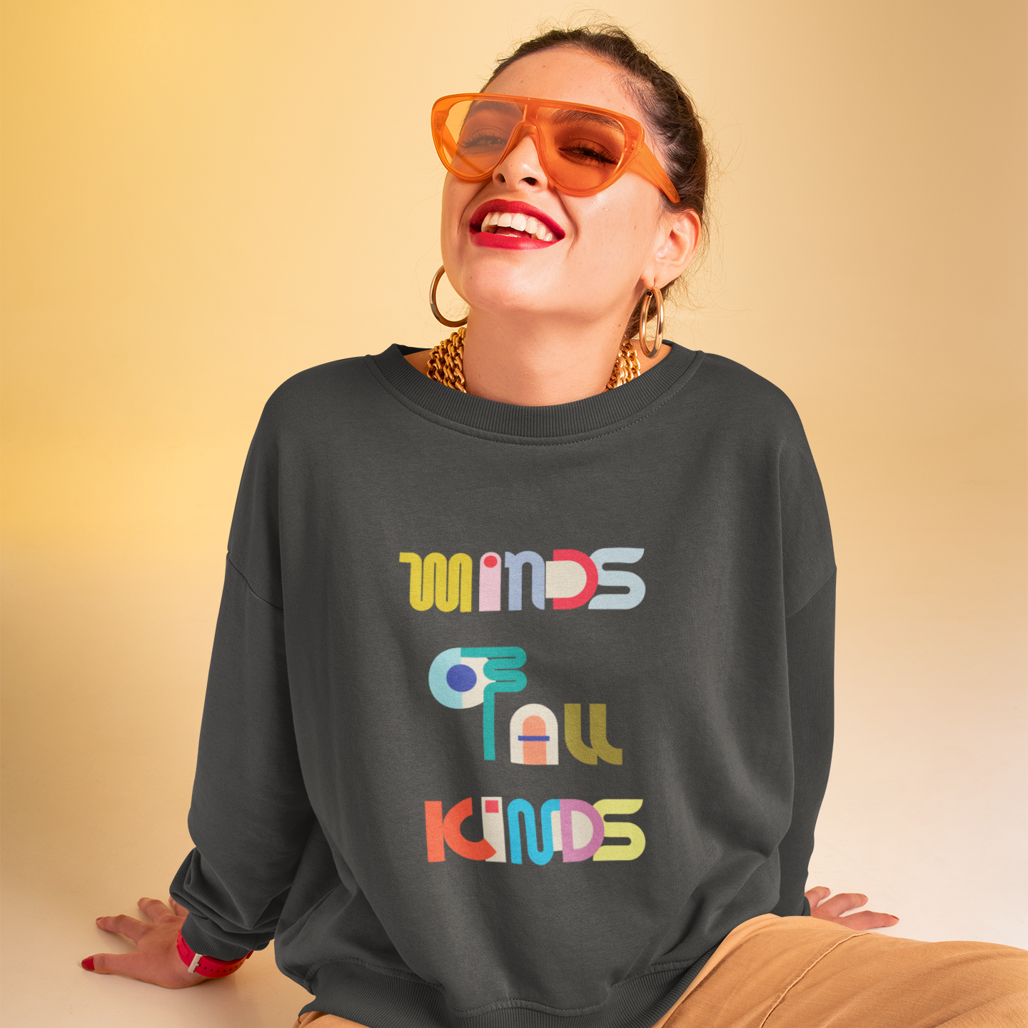 Person wearing a dark gray sweatshirt with colorful text and orange sunglasses on a beige background